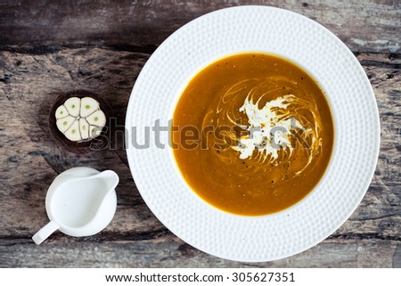 Creamy pumpkin soup - homemade recipe of cream vegetarian dish swirled with coconut milk on a wooden table.