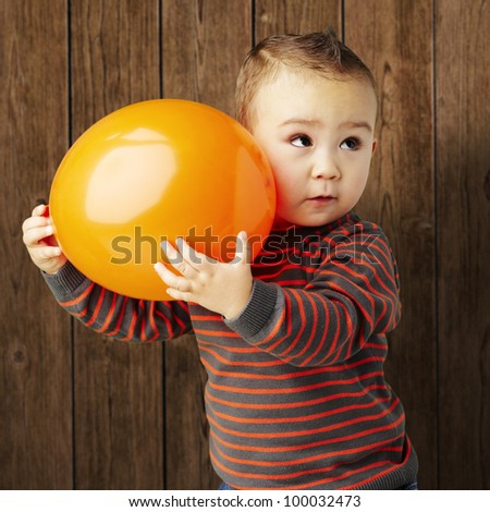 portrait of a funny kid holding a big orange balloon against a wooden background
