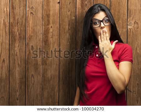 portrait of a young woman covering her mouth with her hand against a wooden wall