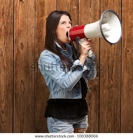 portrait of a young woman screaming with a megaphone against a wooden wall
