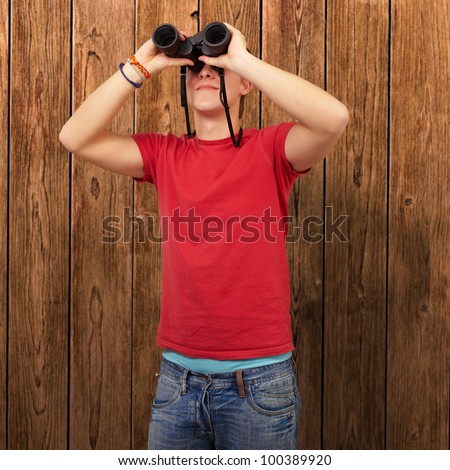 portrait of a young man with binoculars against a wooden wall