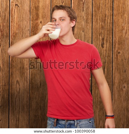 portrait of a young man drinking milk against a wooden wall