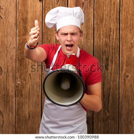 portrait of a young cook man screaming with a megaphone and gesturing against a wooden wall