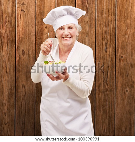 portrait of an adorable senior cook woman eating a salad against a wooden wall