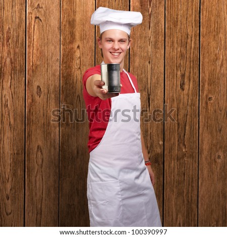 portrait of a young cook man holding a metal tin can against a wooden wall