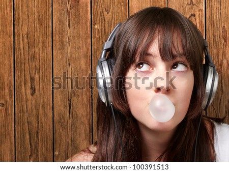 portrait of a young woman listening to music with bubble gum against a wooden wall