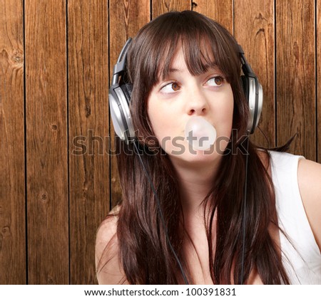portrait of a young woman listening to music with bubble gum against a wooden wall