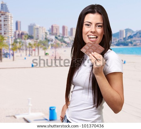 portrait of young woman eating chocolate bar against a beach