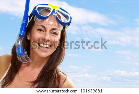 portrait of a happy middle aged woman wearing snorkel and goggles against a blue sky