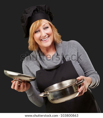 Middle aged cook woman holding a sauce pan over a black background