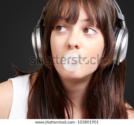 portrait of a young woman listening to music with bubble gum over a black background