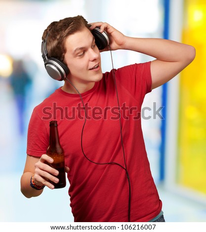 portrait of a young man listening to music and holding a beer indoor