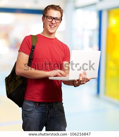 portrait of a young man holding a laptop and wearing a backpack indoor