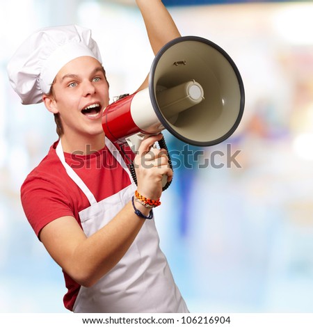 portrait of a young cook man shouting with a megaphone indoor