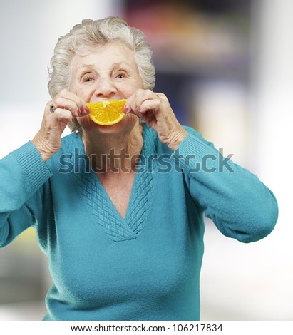 portrait of a senior woman holding an orange slice in front of her mouth, indoor