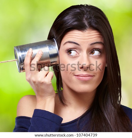 portrait of a young woman hearing through a tin can against a nature background
