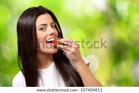 portrait of a young woman eating a strawberry against a nature background