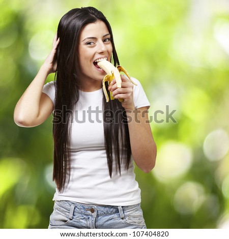 young woman eating a banana against a nature background