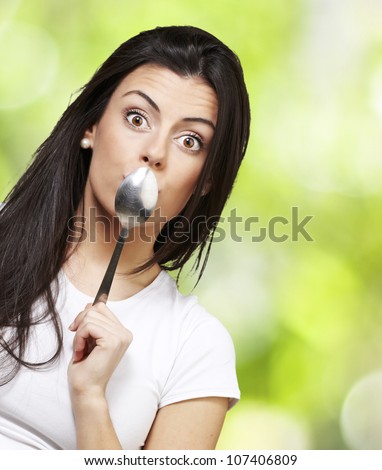woman covering her mouth with a spoon against a nature background