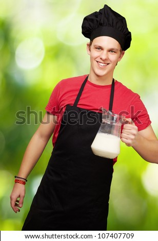 portrait of a young cook man holding a milk jar against a nature background