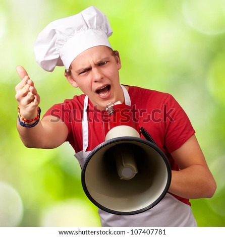 portrait of a young cook man screaming with a megaphone and gesturing against a nature background