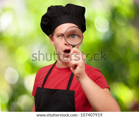 portrait of a young cook man looking through a magnifying glass against a nature background