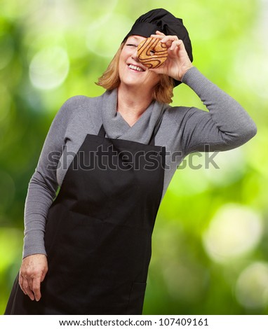 Middle aged cook woman looking through a donut against a nature background