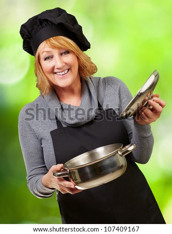 Middle aged cook woman holding a sauce pan against a nature background
