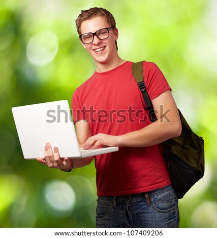 portrait of a young man holding a laptop and wearing a backpack against a nature background