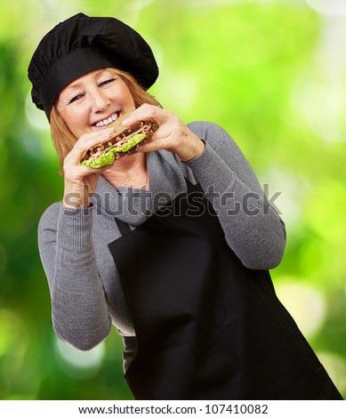 Middle aged cook woman holding a vegetable sandwich against a nature background