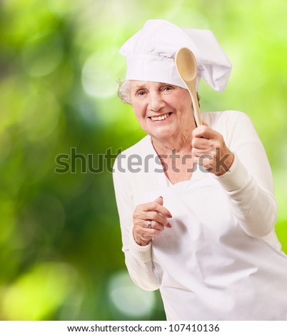 portrait of a senior cook woman holding a wooden spoon against a nature background