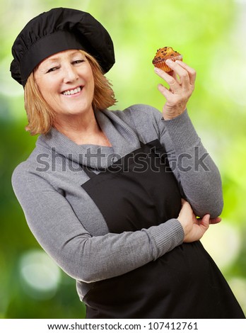 portrait of a middle aged cook woman holding a homemade muffin against a nature background