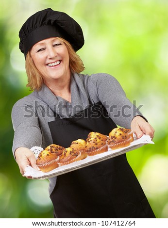 portrait of a cook woman showing a homemade muffin tray against a nature background
