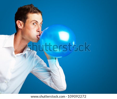 Portrait Of Young Man BlowingÃ?Â Balloon On Blue Background