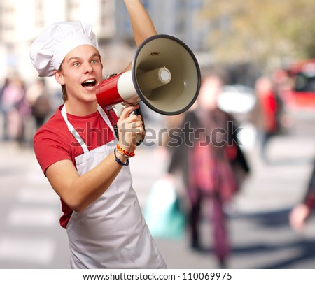 portrait of young cook man shouting with megaphone at crowded street