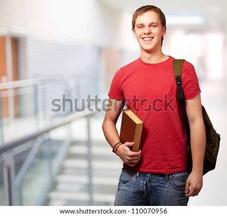 portrait of young student holding book and carrying backpack at university