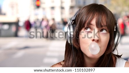 portrait of young woman listening to music with bubble gum against a crowded city