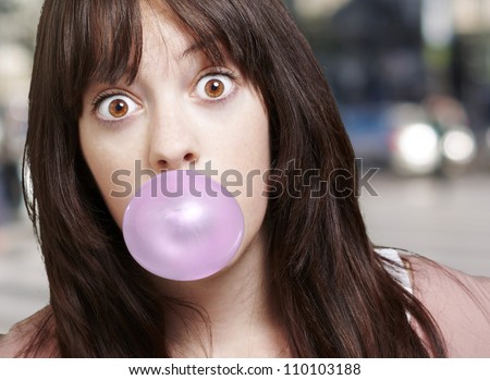 young girl with a pink bubble of chewing gum against a street background