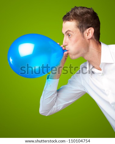 Portrait Of Young Man Blowing A Balloon Isolated On Green Background
