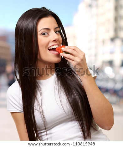 portrait of young woman eating strawberry at city