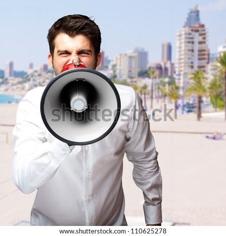 portrait of young man screaming with megaphone against a beach