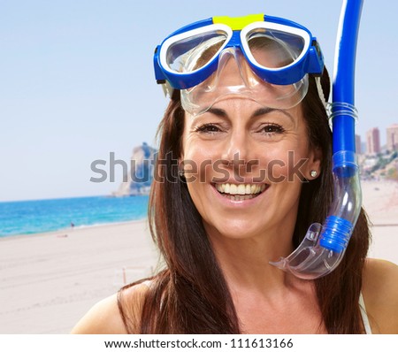 portrait of a happy middle aged woman wearing snorkel and goggles against the beach