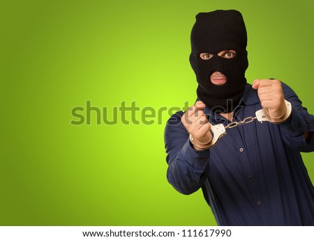 angry criminal man locked in handcuffs isolated on green background