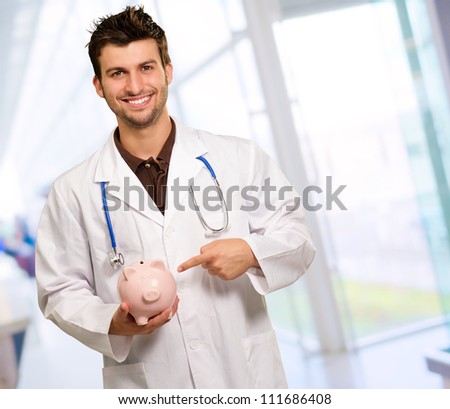 Portrait Of A Young Doctor Holding A Piggy Bank, Indoor