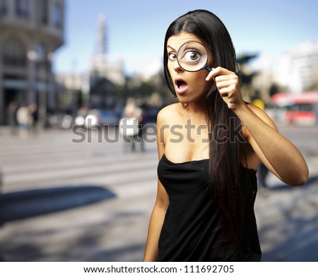 Young woman surprised looking through a magnifying glass at city
