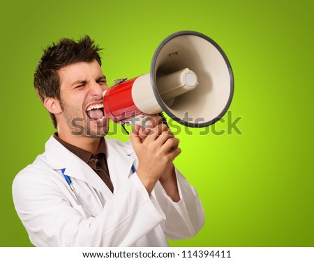 Portrait Of A Male Doctor Shouting On Megaphone On Green Background