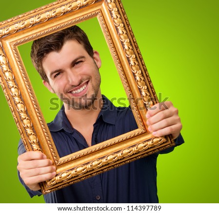 A Young Man Holding And Looking Through Frame On Green Background