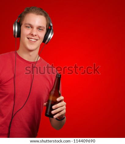 portrait of young man listening music and holding beer over red background