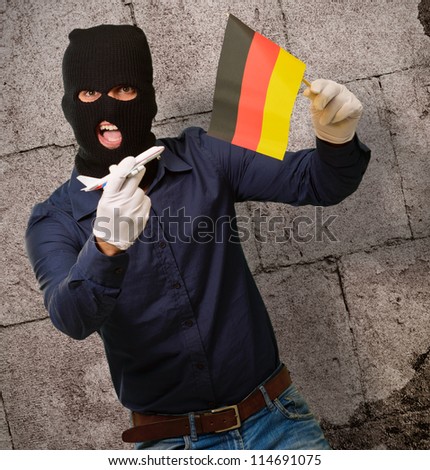 Man wearing a robber mask and holding airplane miniature and flag, indoor