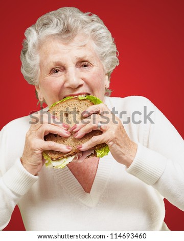 portrait of senior woman eating vegetable sandwich over red background